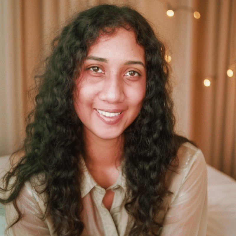 A smiling picture of me sitting at a desk in a modern office in a cream colored blouse